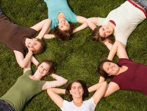 people laying on backs in a grass field forming a circle